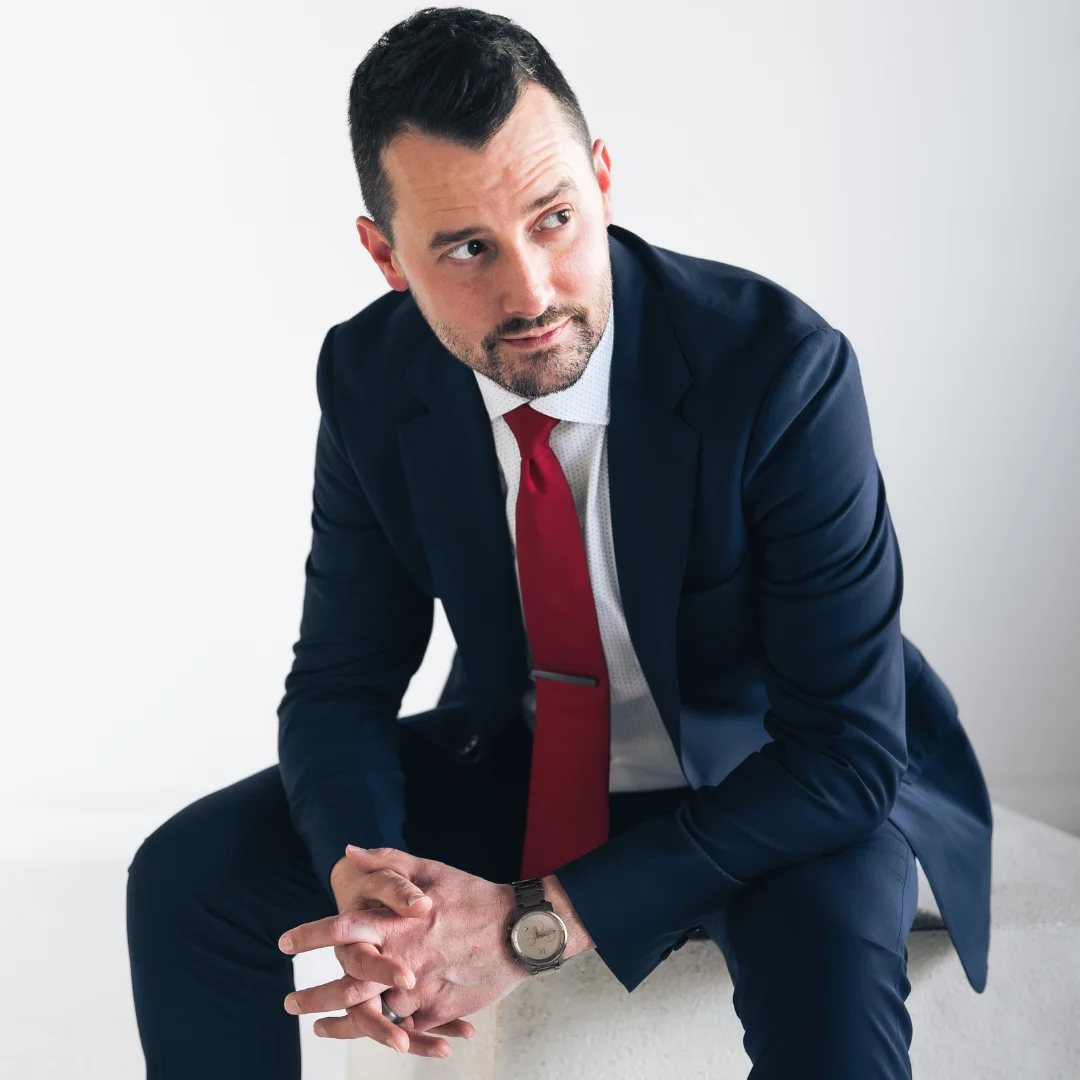 Josh Fletcher in a suit with a red tie sitting on a white background