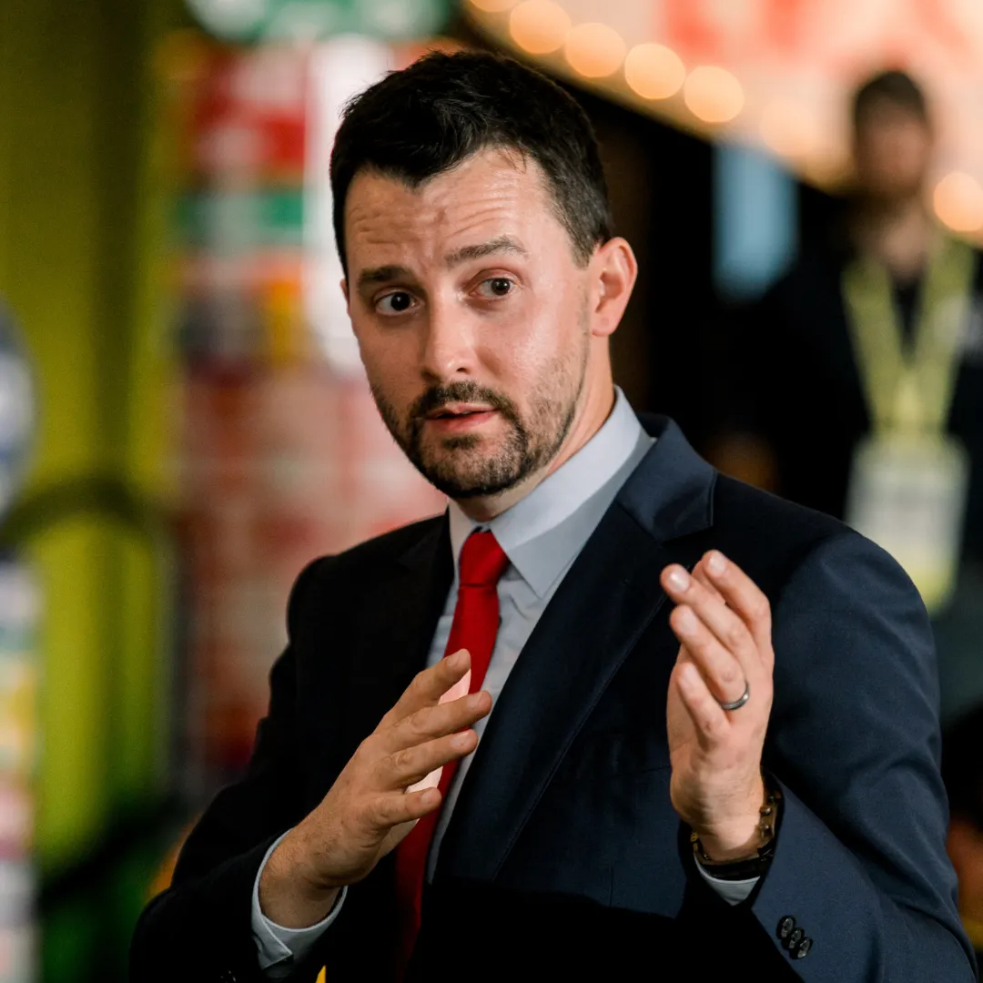 Josh Fletcher speaking at an event in a suit and red tie